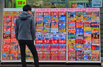 Standing Man Wearing Gray Hoodie in Front of Magazine in Rack