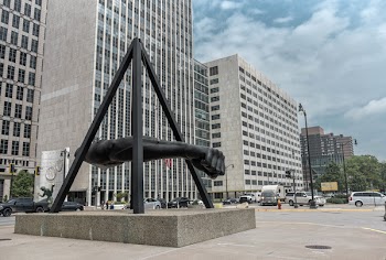 Statue of Human Arm Near Gray Buildings