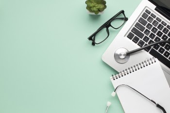 Stethoscope; spiral diary; spectacle and succulent plant with laptop on green background Free Photo