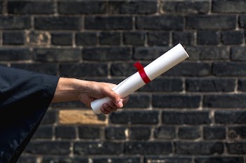 Student Holding Out Diploma By Wall