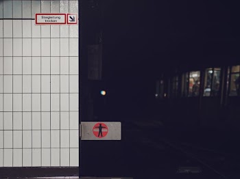 Subway train in a dark underground train station near a tiled wall with a warning sign