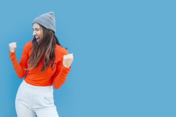 Successful happy young woman with clenching fists in front of blue surface Free Photo