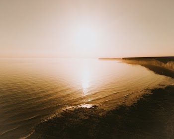 Sun Glaring Over Calm Water Of The Sea And Its Surrounding Landscape
