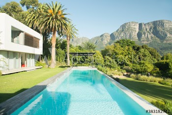 Sunny tranquil swimming pool outside luxury house below mountain