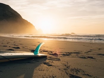 surfboard on brown sand beside ocean during sunset