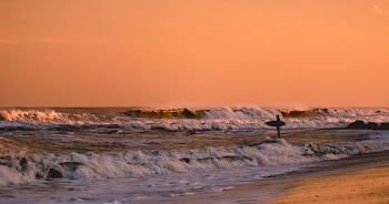 Surfer standing in shallow water, looking at waves at sunset in Bradley Beach