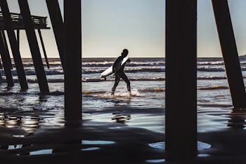 Surfer Walks Near Dock at the Beach