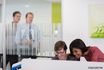 Suspicious businessmen watching businesswomen laughing in office