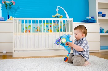Sweet baby boy ( 1 year old ) sitting on floor at home and playing with soft toys at children's room.