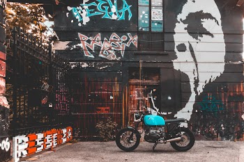 Teal Cafe Racer Motorcycle Parked Next to Black and Multicolored Painted Building