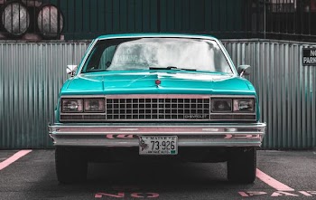 teal Chevrolet car parked on asphalt road near trailers
