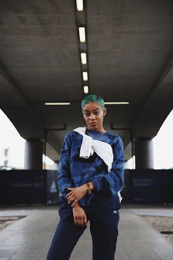 teal-haired woman standing under concrete bridge