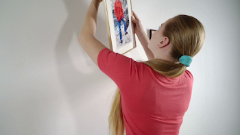 Teenage girl hanging family framed photos on wall at home holding ...