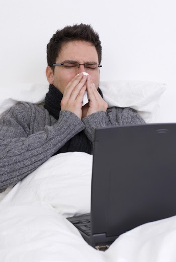 The man sneezing, working at home on the bed