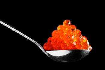 The spoon with red caviar on a black background