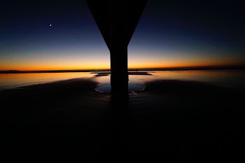 The sun-kissed horizon looms behind the pillar and across the water at dusk at New Brighton
