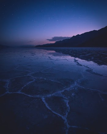 The very first light of dawn illuminates Badwater Basin under a starlit sky in Death Valley National Park, California, USA.