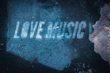 The words LOVE MUSIC stencilled and spray painted on a wall that is crumbling and exposing the concrete beneath the surface.