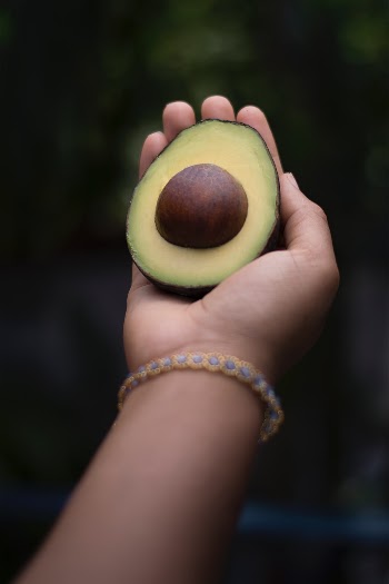 This image/photo is of a young beautiful black melanin woman's hand holding an exotic fruit called an Avocado. The strong black woman is also wearing a hand-made bracelet from Mexico.