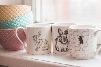 Three Assorted-design Ceramic Mugs next to a Pile of Ceramic Bowls