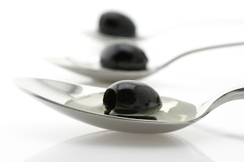 Three black olives in spoons with oil on white background..