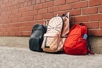 Three Children's Backpacks And A Brick Wall