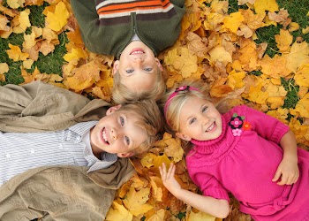three cute caucasian kids lying on fall leaves outdoors