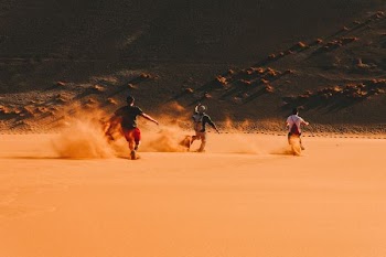 three men running on desert during daytime