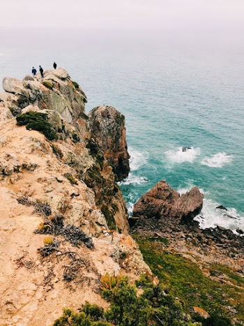 Three Men Standing on Top of Cliff in Beach