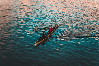 Three People on Brown Canoe Sailing on Calm Water