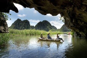 Three People Sitting on Boat While Sailing Under Cave