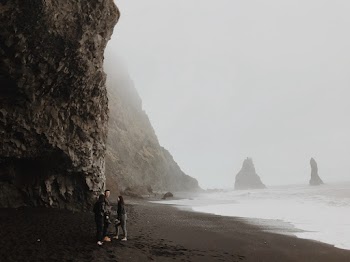 Three People Standing Near Seashore Viewing Cliff Covered With Fogs
