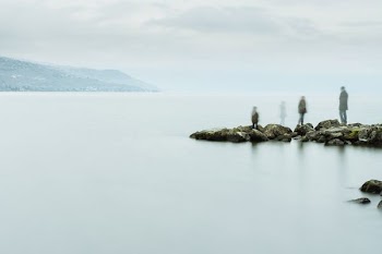 three people standing on boulders near body of water
