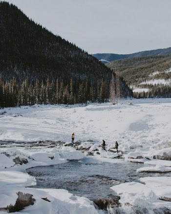 three people standing on snow near body of water during daytim