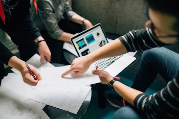 three people surrounding paper and laptop inside room