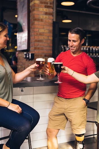 Three People Toasting Their Beers in Front of the Bar