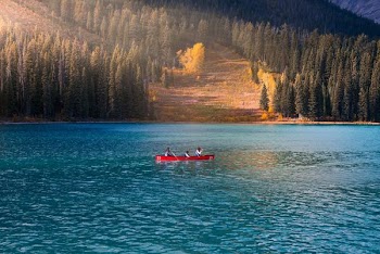 three person in red rowboat on blue calm body of water at daytime