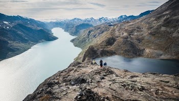 three person on rocky mountain beside river under white sky during daytime
