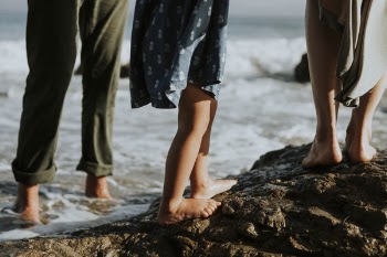 Three Person Standing on Rock Monolith Beside Sand Beach