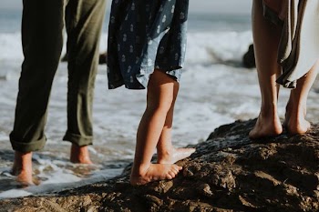 three person standing on rock near seashore