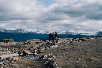 three person standing under white cloudy sky facing on snow covered mountain during daytime