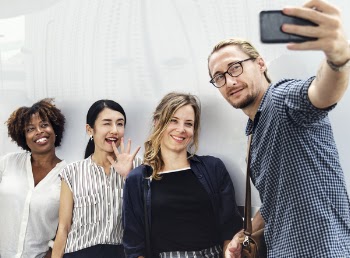 Three Smiling Women Beside Man Holding Smartphone