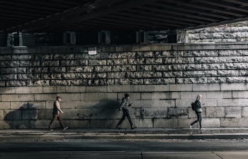 Three Urban Pedestrians Walk Under Bridge