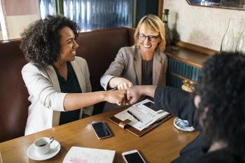 Three Woman Sitting on Brown Leather Padded Bench While Fistbump