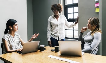 Three Woman Talking Near Laptop on Desk Inside Room
