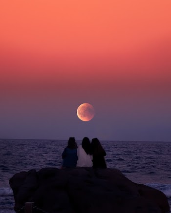 Three Women Sitting on Rock Infront of Ocean