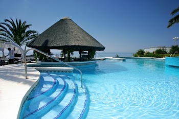 Tiki hut and bar by steps of swimming pool of luxury hotel on a bright sunny day in Spain