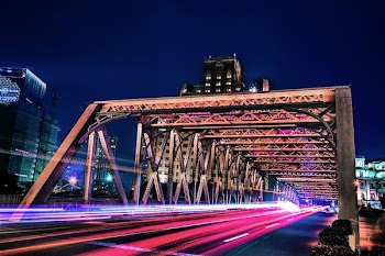 time lapse and light streaks photo of vehicle on bridge with high rise buildings in distant