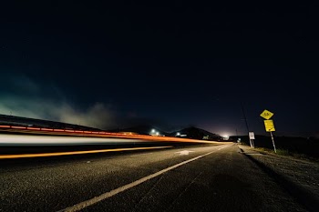 timelapse photo of red vehicle on gray asphalted road under black sky