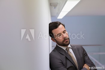 Tired corporate businessman leaning against wall with eyes closed